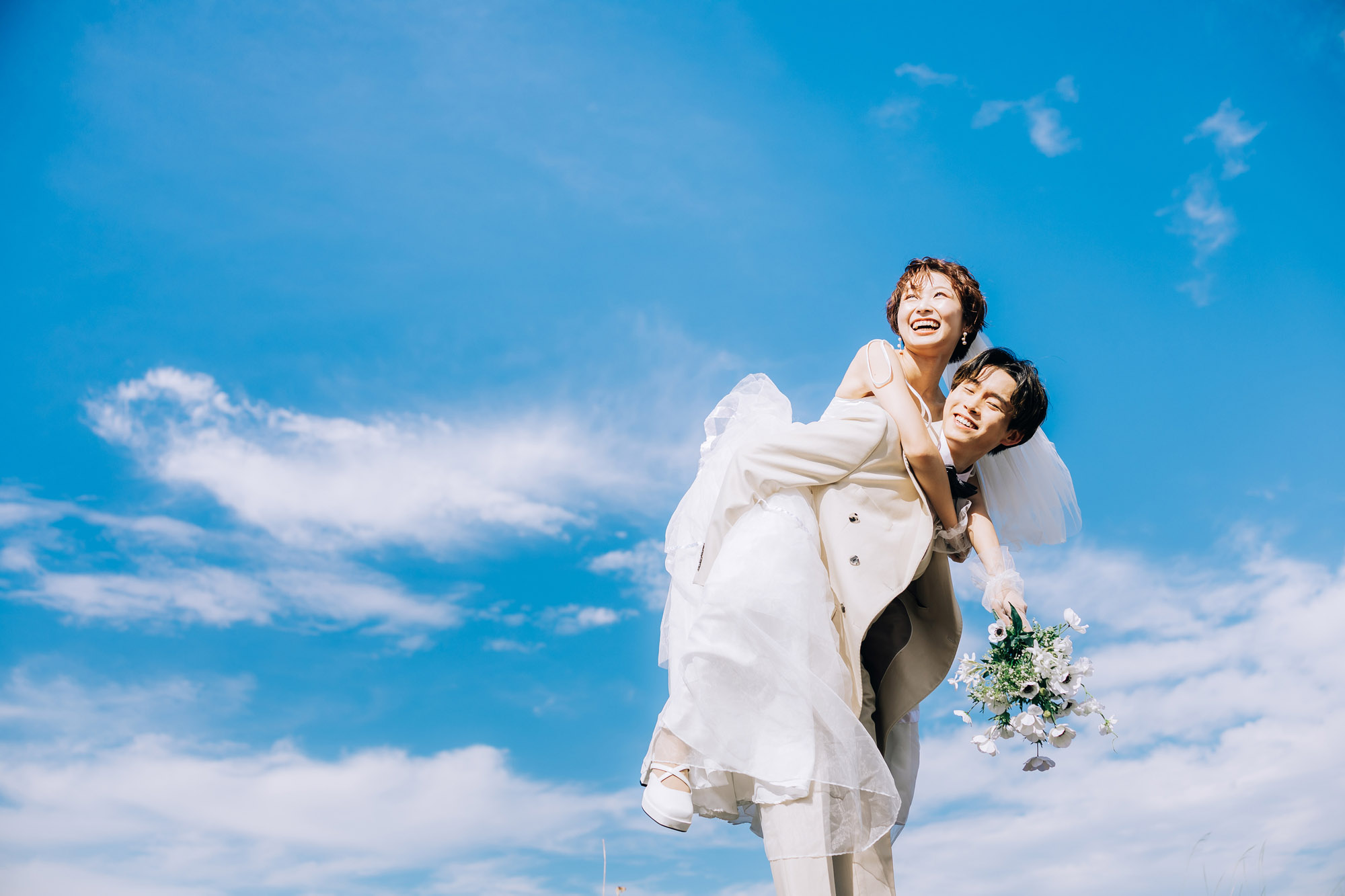 青空の下で笑顔を見せる新郎新婦